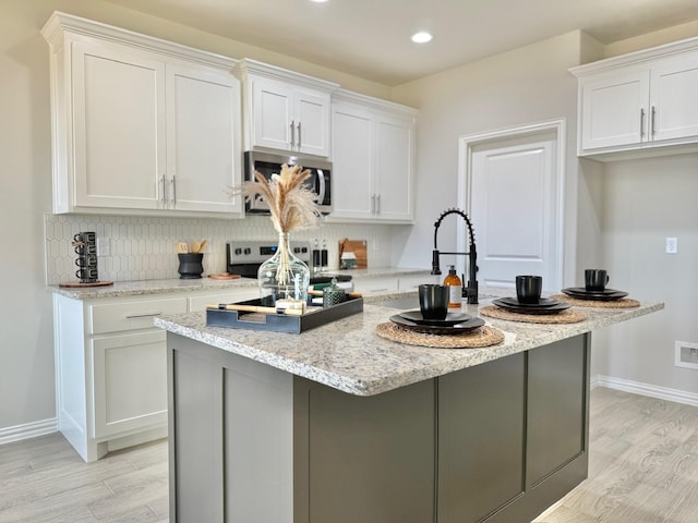 kitchen with stainless steel appliances, white cabinetry, and a center island with sink