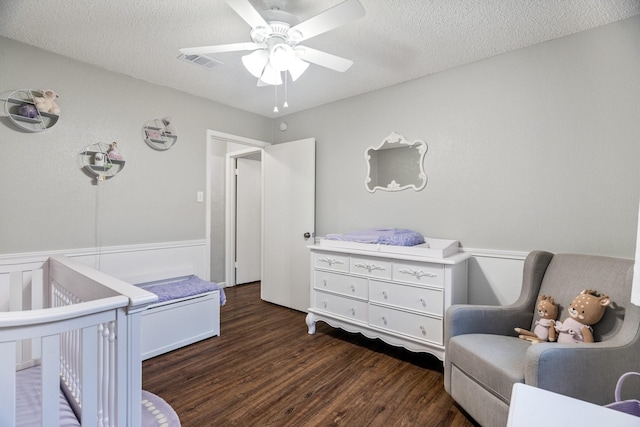 bedroom featuring a crib, ceiling fan, dark wood-type flooring, and a textured ceiling