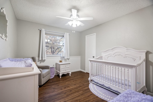 bedroom with dark hardwood / wood-style flooring, ceiling fan, a nursery area, and a textured ceiling