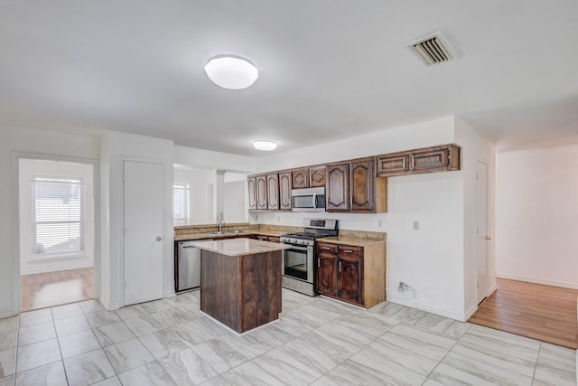 kitchen featuring appliances with stainless steel finishes, sink, a center island, dark brown cabinetry, and light stone countertops