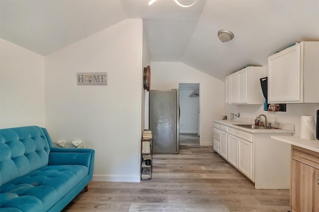 kitchen featuring sink, white cabinetry, vaulted ceiling, light hardwood / wood-style flooring, and stainless steel fridge