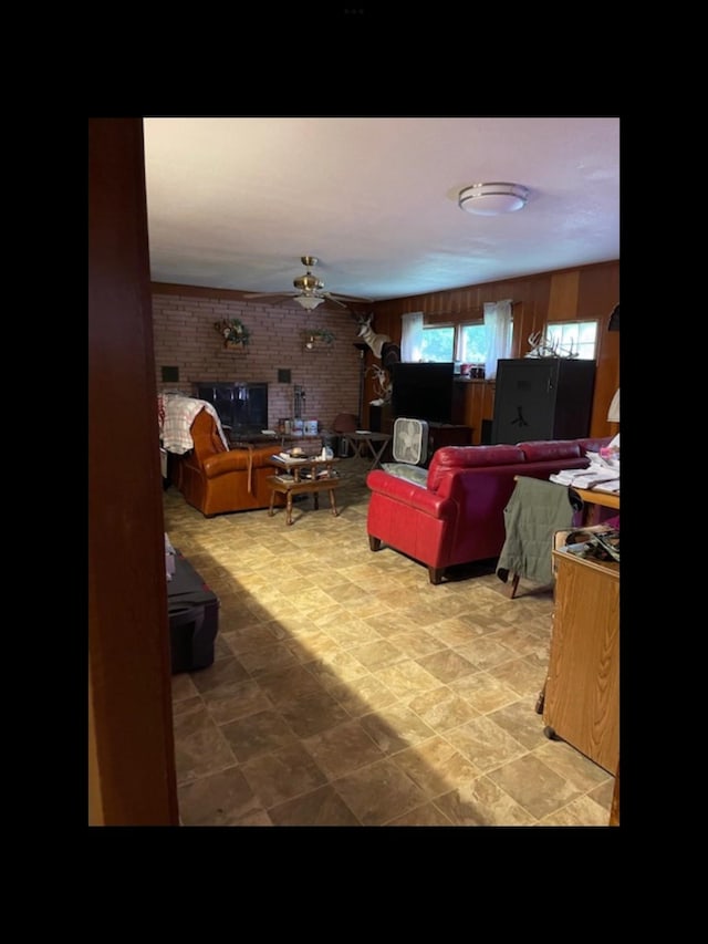 living room with a brick fireplace, ceiling fan, and brick wall