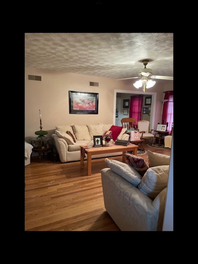 living room with ceiling fan, wood-type flooring, and a textured ceiling