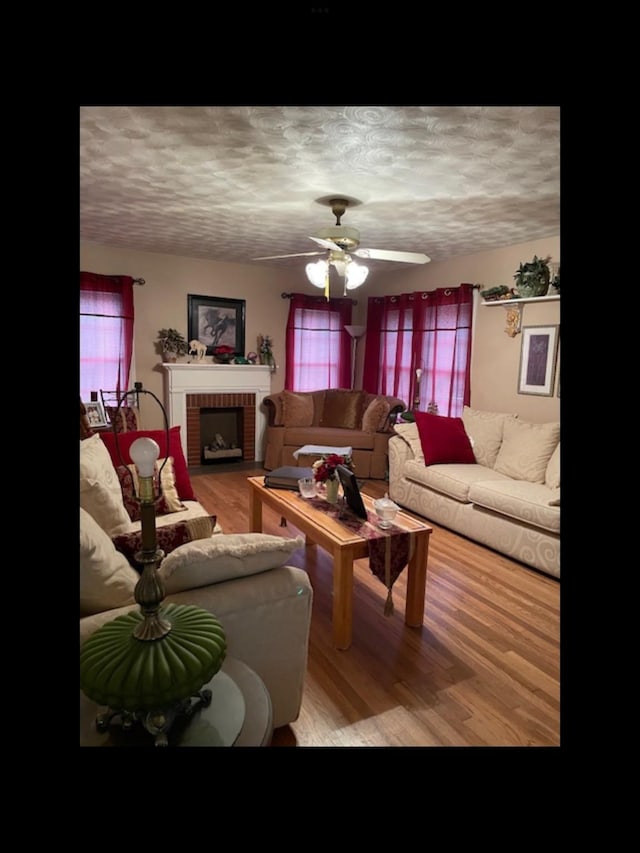 living room featuring ceiling fan, a fireplace, a textured ceiling, and light wood-type flooring