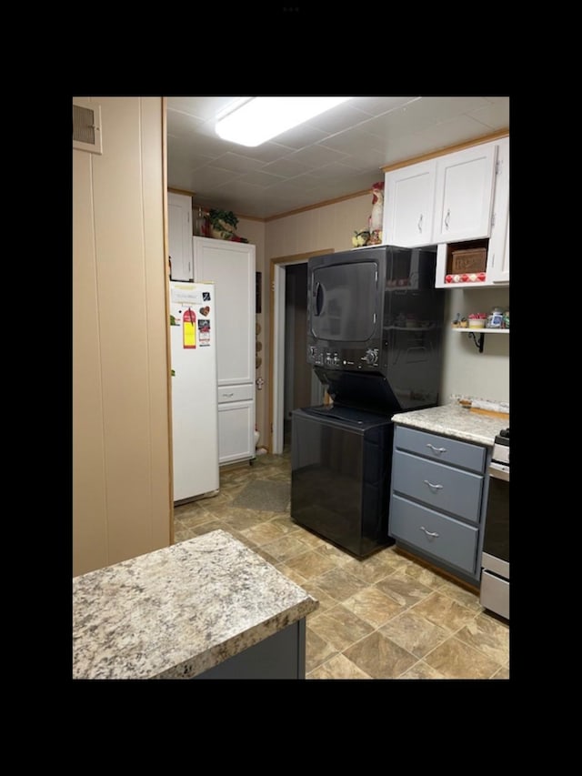 kitchen with stacked washing maching and dryer, stainless steel range with gas cooktop, gray cabinetry, white cabinets, and white refrigerator