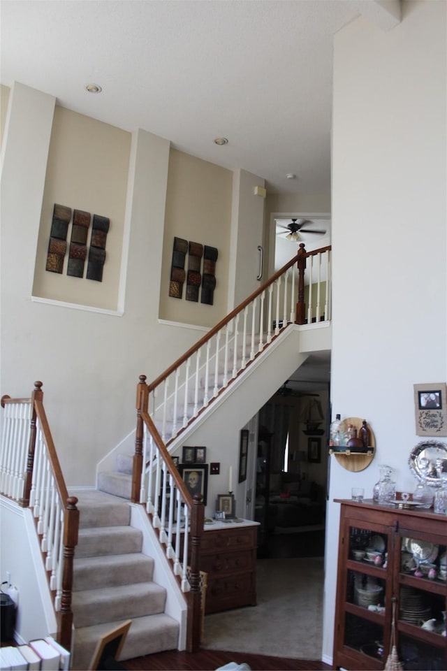 stairway featuring carpet floors, ceiling fan, and a high ceiling