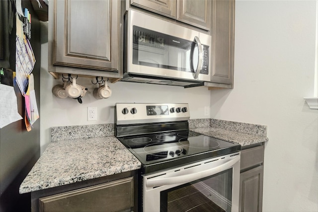 kitchen with dark brown cabinetry, appliances with stainless steel finishes, and light stone counters