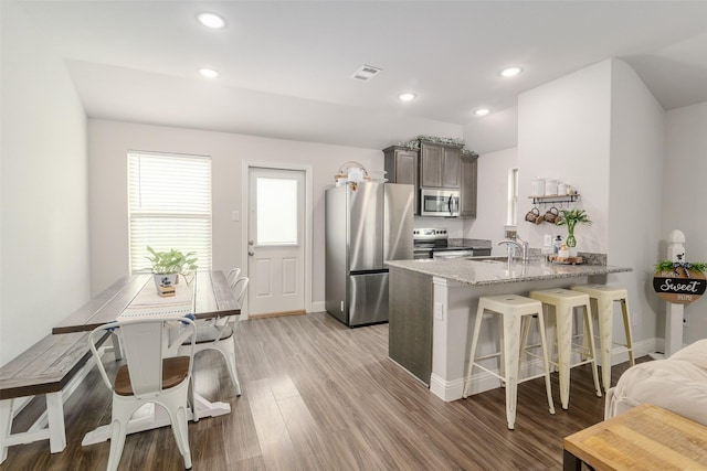 kitchen featuring a breakfast bar area, light stone counters, appliances with stainless steel finishes, kitchen peninsula, and light hardwood / wood-style floors