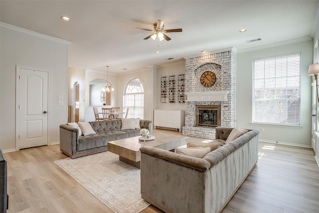 living room with ornamental molding, a brick fireplace, ceiling fan with notable chandelier, and light hardwood / wood-style floors