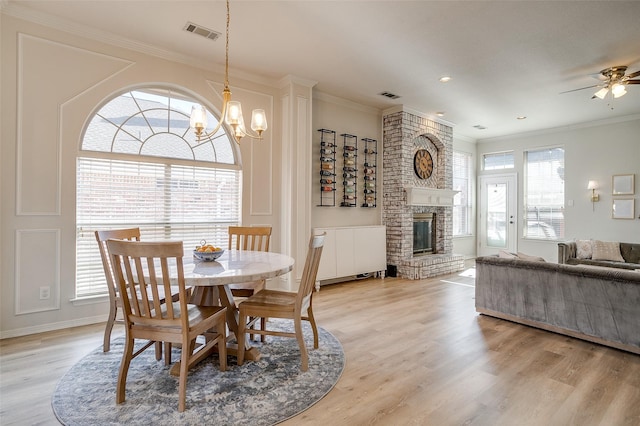 dining area featuring ceiling fan with notable chandelier, a fireplace, ornamental molding, and light hardwood / wood-style floors