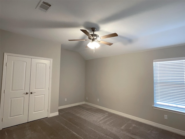 unfurnished bedroom featuring dark carpet, vaulted ceiling, a closet, and ceiling fan