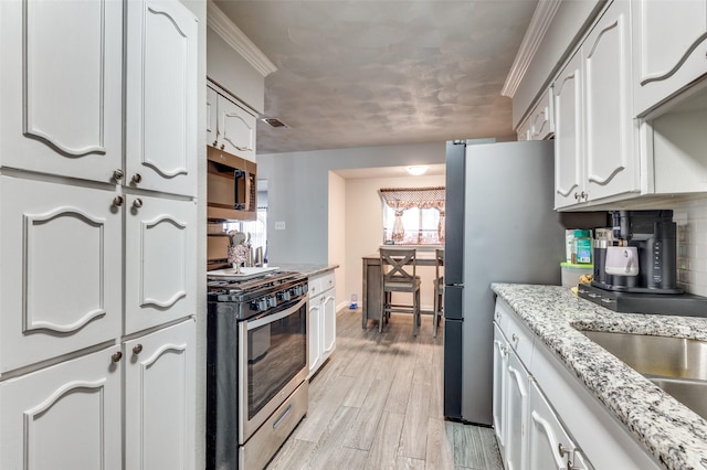 kitchen with ornamental molding, appliances with stainless steel finishes, white cabinets, and light hardwood / wood-style flooring