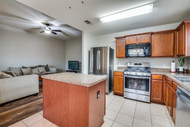 kitchen featuring light tile patterned flooring, ceiling fan, appliances with stainless steel finishes, and a center island