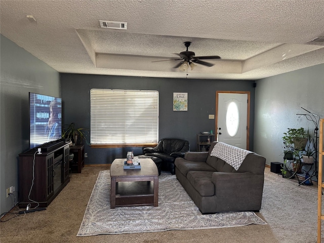 carpeted living room featuring a textured ceiling, ceiling fan, and a tray ceiling