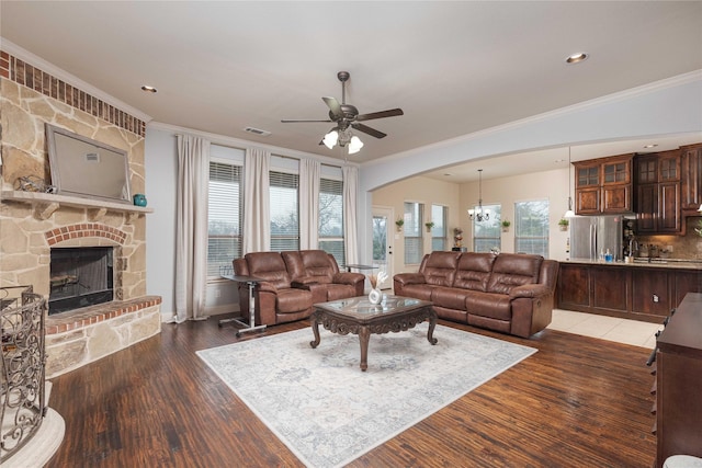 living room with dark hardwood / wood-style flooring, crown molding, a fireplace, and ceiling fan with notable chandelier