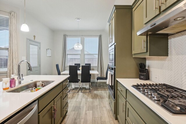 kitchen featuring sink, green cabinetry, pendant lighting, stainless steel appliances, and decorative backsplash