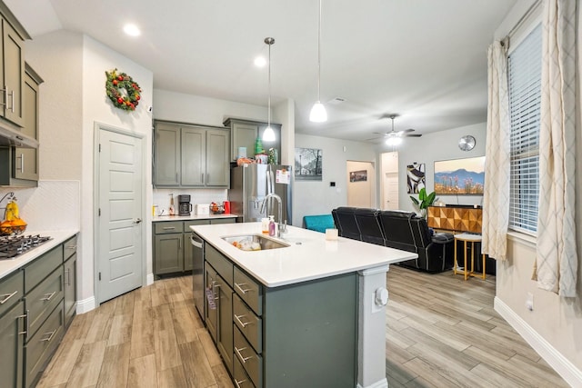 kitchen with pendant lighting, sink, stainless steel appliances, light hardwood / wood-style floors, and an island with sink