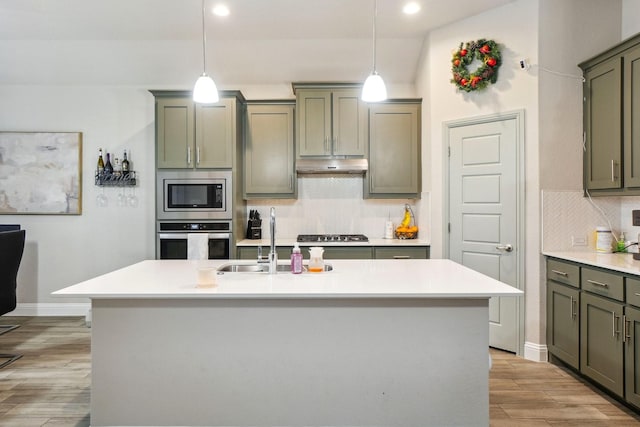 kitchen featuring pendant lighting, tasteful backsplash, sink, stainless steel appliances, and a center island with sink