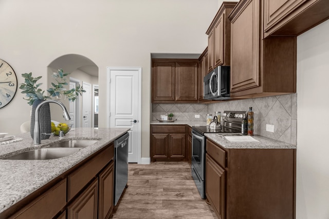 kitchen with sink, light stone counters, appliances with stainless steel finishes, hardwood / wood-style floors, and decorative backsplash