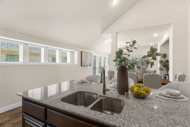 kitchen with vaulted ceiling, dark wood-type flooring, light stone countertops, and sink