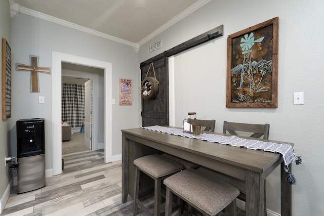 dining area featuring crown molding, light hardwood / wood-style floors, and a barn door