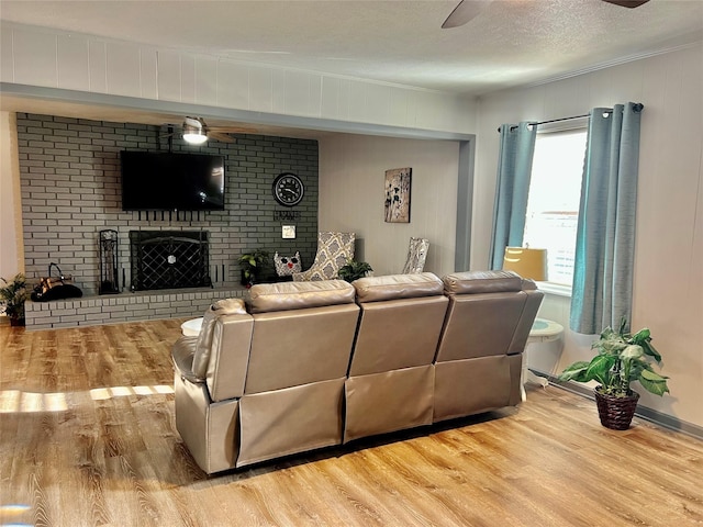 living room featuring a brick fireplace, a textured ceiling, ceiling fan, and light wood-type flooring