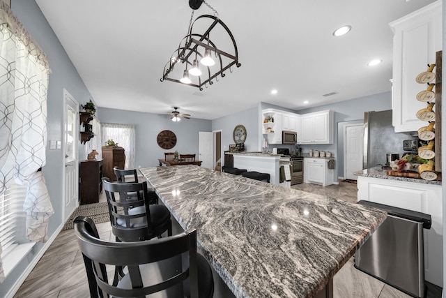 kitchen with a kitchen island, white cabinetry, appliances with stainless steel finishes, and light stone counters