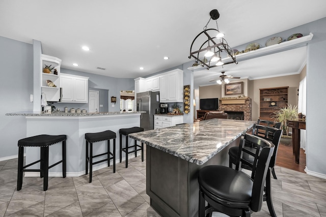 kitchen with ceiling fan, white cabinetry, stainless steel refrigerator with ice dispenser, light stone countertops, and kitchen peninsula