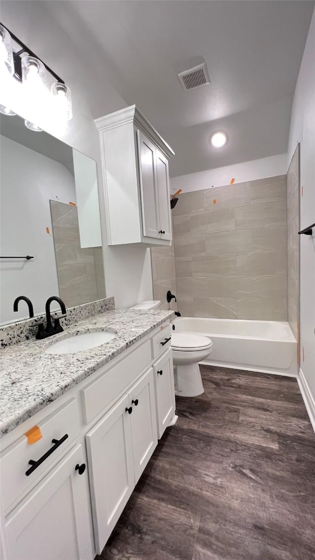 full bathroom featuring vanity, tiled shower / bath combo, wood-type flooring, and toilet