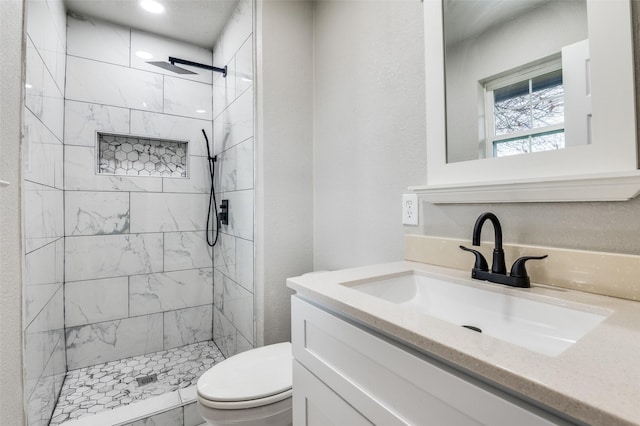 bathroom with tiled shower, vanity, and toilet