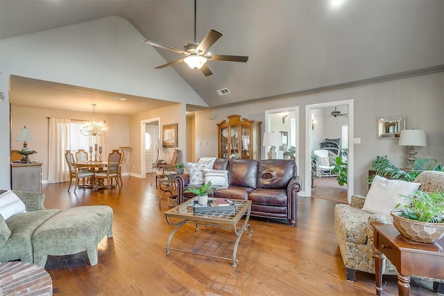 living room with ceiling fan with notable chandelier, high vaulted ceiling, and hardwood / wood-style floors