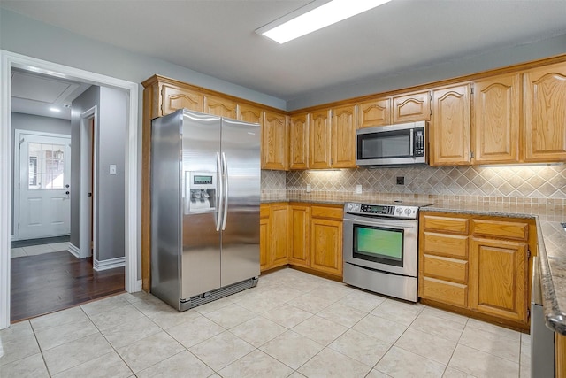 kitchen featuring light tile patterned flooring, appliances with stainless steel finishes, light stone countertops, and decorative backsplash