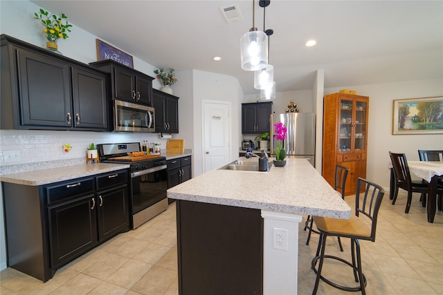 kitchen featuring pendant lighting, sink, backsplash, stainless steel appliances, and a center island with sink