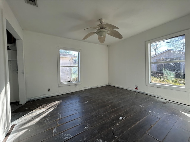 empty room with a healthy amount of sunlight, dark wood-type flooring, and ceiling fan