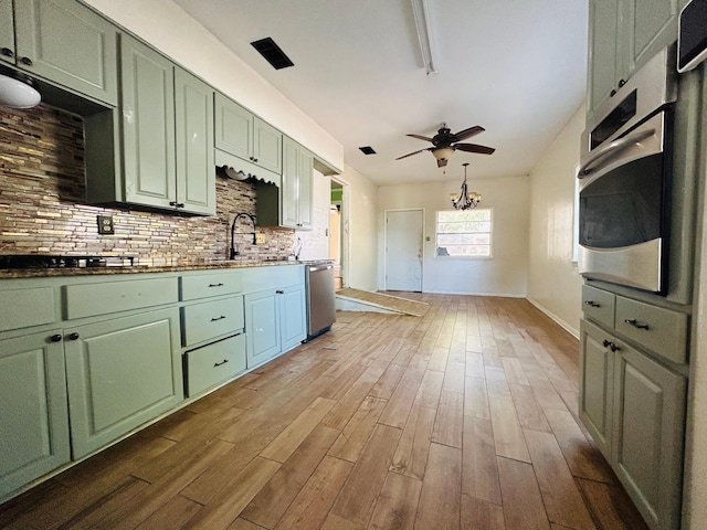 kitchen with sink, green cabinetry, light wood-type flooring, appliances with stainless steel finishes, and decorative backsplash