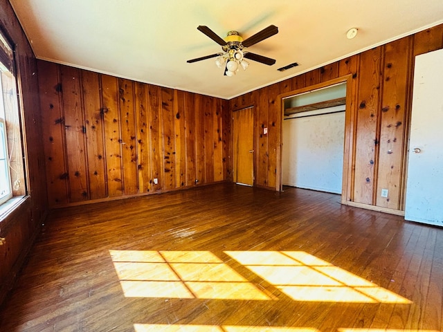 unfurnished bedroom with dark hardwood / wood-style flooring, wooden walls, and ceiling fan