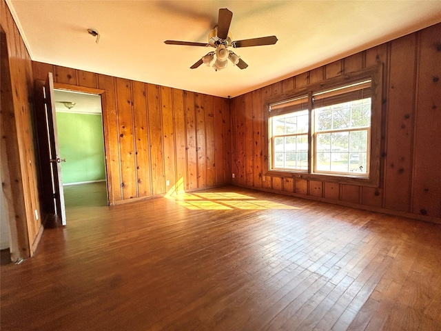 empty room featuring ceiling fan, hardwood / wood-style floors, and wood walls