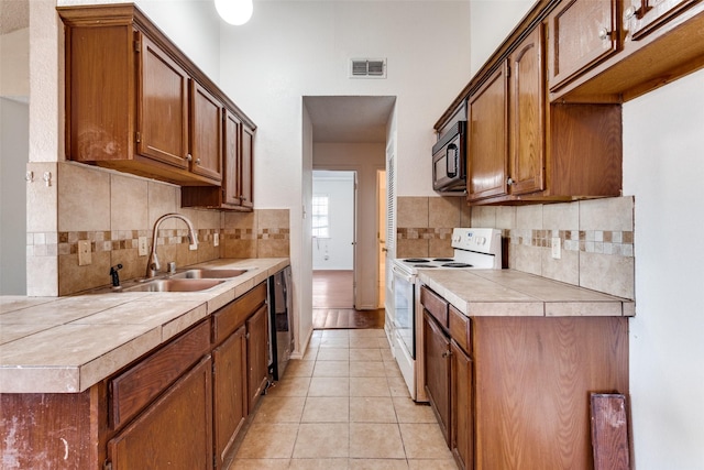 kitchen with light tile patterned flooring, sink, decorative backsplash, tile counters, and black appliances