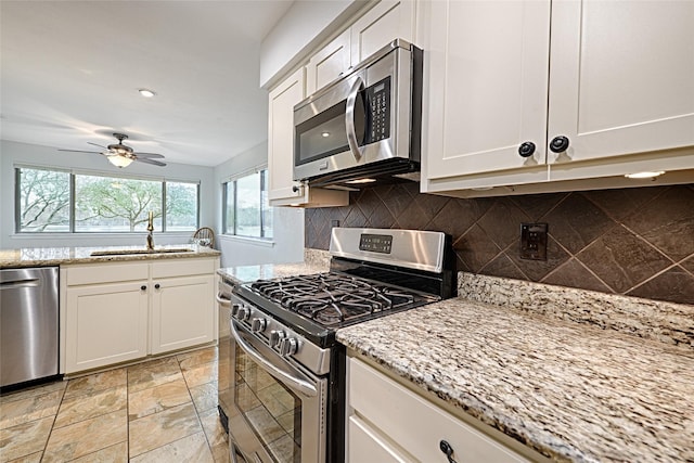 kitchen with appliances with stainless steel finishes, a sink, white cabinetry, and light stone countertops