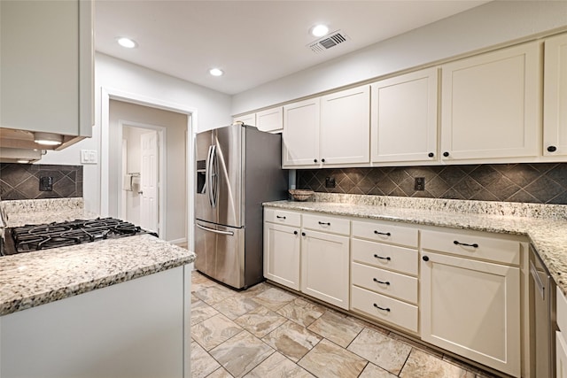 kitchen featuring visible vents, stove, stainless steel refrigerator with ice dispenser, and light stone countertops