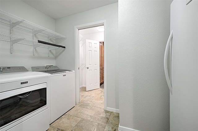 washroom with a textured wall, stone finish floor, separate washer and dryer, laundry area, and baseboards