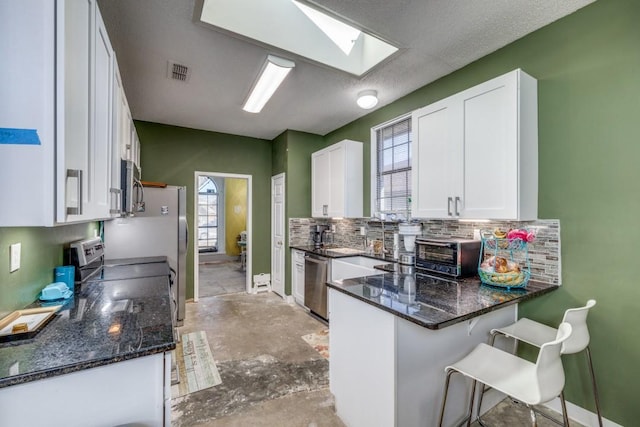 kitchen featuring white cabinetry, decorative backsplash, dark stone counters, kitchen peninsula, and stainless steel appliances