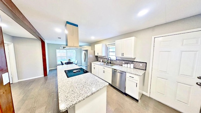 kitchen with sink, stainless steel appliances, light stone counters, white cabinets, and a kitchen island