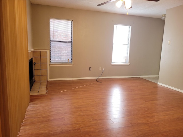 empty room with ceiling fan, a fireplace, and light hardwood / wood-style flooring