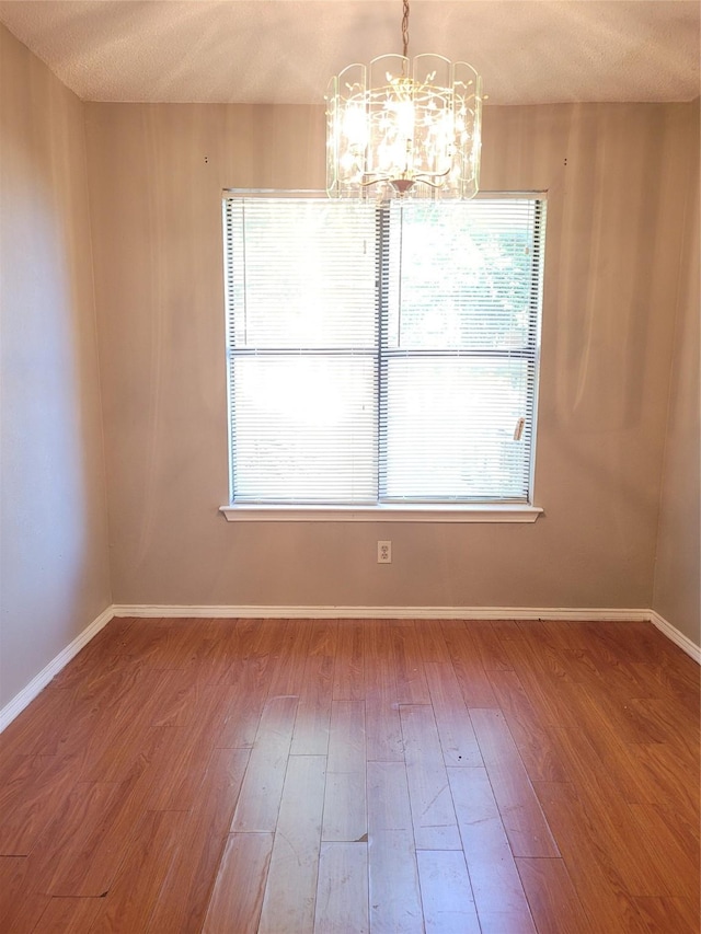 empty room with an inviting chandelier, wood-type flooring, and a wealth of natural light