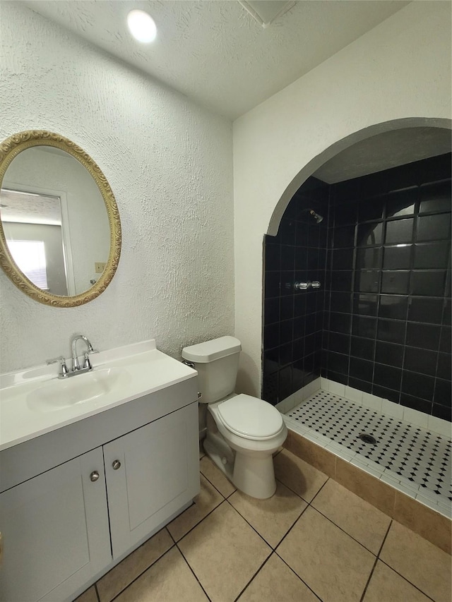 bathroom with toilet, a textured ceiling, a tile shower, vanity, and tile patterned flooring