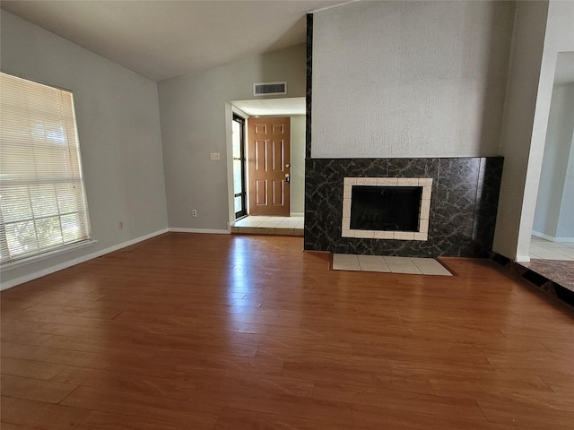 unfurnished living room featuring lofted ceiling, hardwood / wood-style flooring, and a tile fireplace