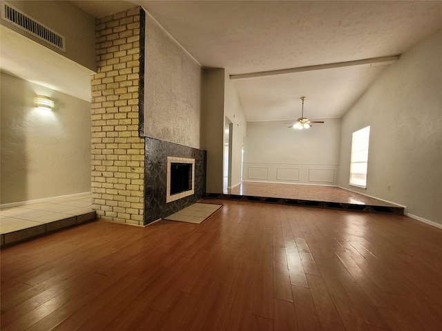 unfurnished living room featuring ceiling fan, wood-type flooring, a tile fireplace, and vaulted ceiling with beams