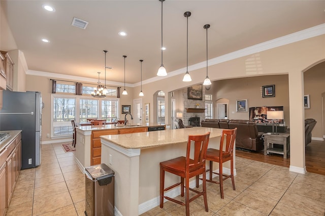 kitchen with pendant lighting, stainless steel refrigerator, a kitchen bar, a kitchen island with sink, and light stone countertops