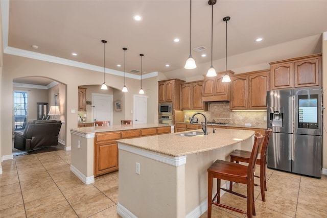 kitchen with appliances with stainless steel finishes, tasteful backsplash, sink, hanging light fixtures, and a kitchen island with sink